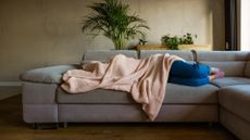 A woman lays on the couch with a blanket over her head