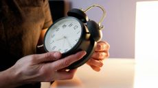 photo of a woman's hands holding a large table-top alarm clock and adjusting the time