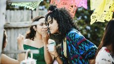 At an outdoor party, a woman whispers in the ear of her friend