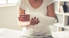 Mid-section of a woman sat down. She has a white medical cast on her left arm which she is supporting with her right hand. 