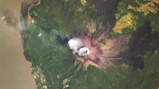 A satellite image of a volcano puffing out a white cloud